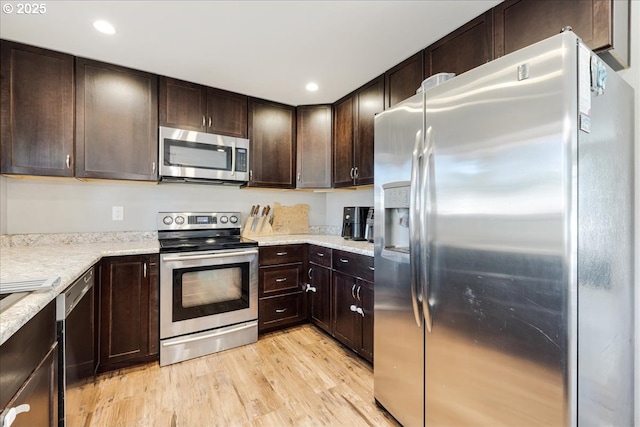 kitchen featuring light stone countertops, appliances with stainless steel finishes, dark brown cabinetry, and light hardwood / wood-style flooring