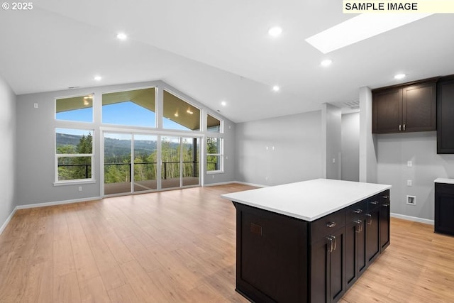 kitchen with dark brown cabinetry, vaulted ceiling with skylight, a center island, and light hardwood / wood-style floors