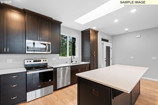 kitchen featuring sink, appliances with stainless steel finishes, a skylight, a center island, and light wood-type flooring