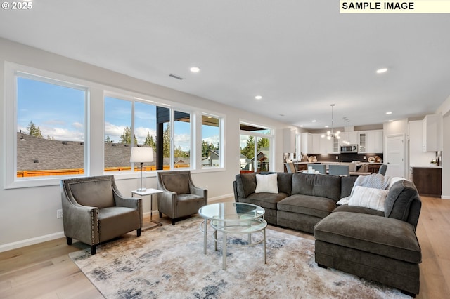 living area with recessed lighting, light wood finished floors, baseboards, and an inviting chandelier