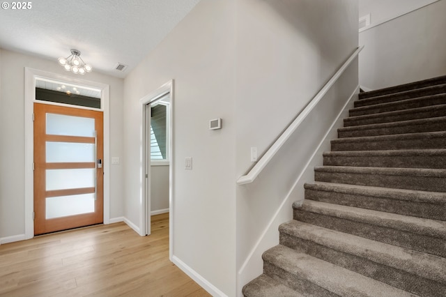 foyer entrance with stairs, a chandelier, light wood-type flooring, baseboards, and visible vents