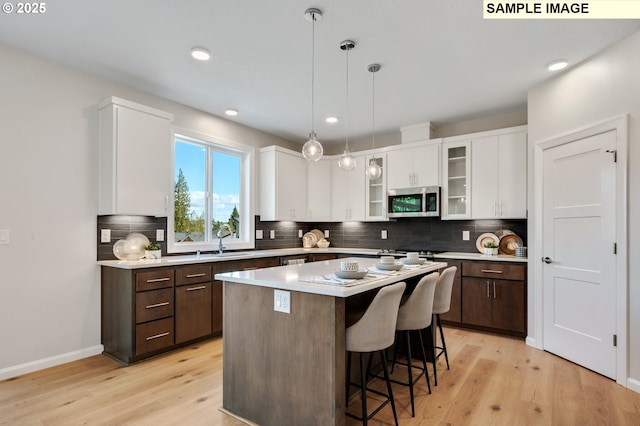 kitchen with white cabinets, light wood finished floors, a sink, stainless steel microwave, and dark brown cabinets
