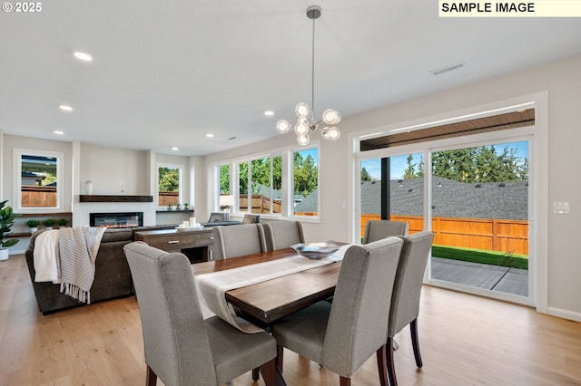 dining space featuring light wood-style flooring, a glass covered fireplace, visible vents, and recessed lighting