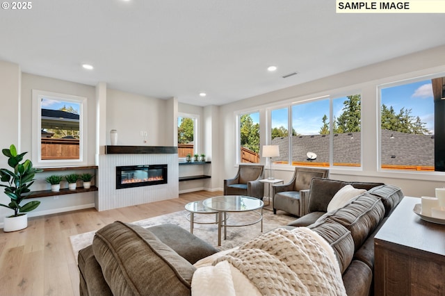 living area with a glass covered fireplace, wood finished floors, visible vents, and recessed lighting