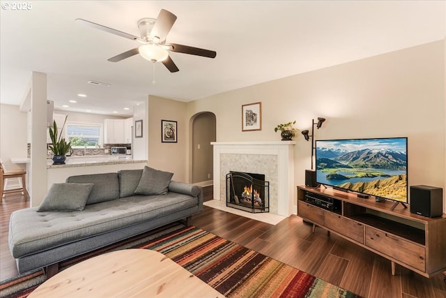 2185 Laurel Ave, Salem, OR 97301 - living room featuring arched walkways, dark wood-style floors, a ceiling fan, a tiled fireplace, and baseboards