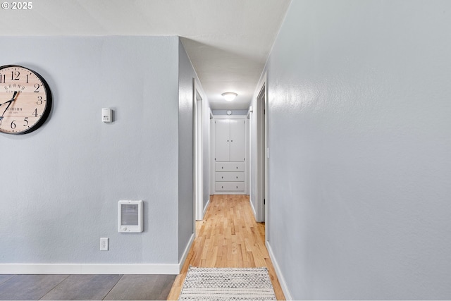 hall with baseboards, light wood-style floors, and heating unit
