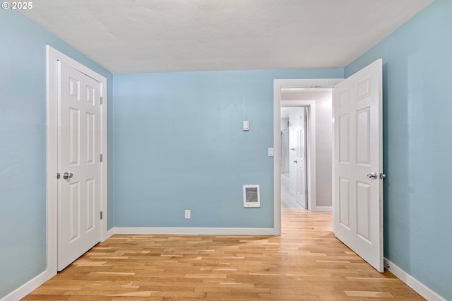 empty room with light wood-type flooring, baseboards, and heating unit