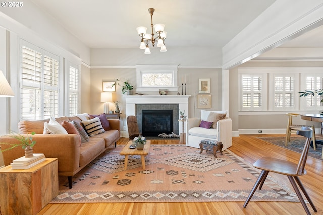 living room featuring an inviting chandelier, a brick fireplace, and wood finished floors