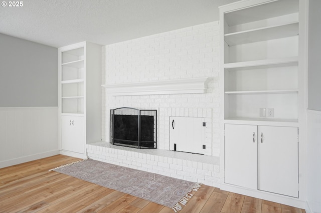 unfurnished living room with a fireplace, light wood-type flooring, a textured ceiling, and built in features