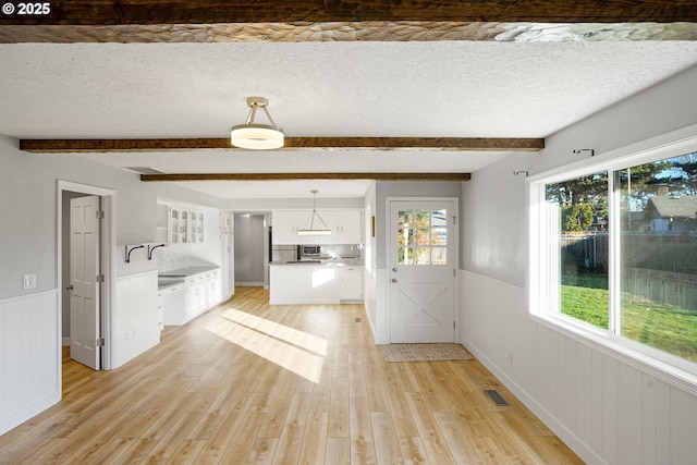 interior space featuring a textured ceiling, beam ceiling, light hardwood / wood-style flooring, and a healthy amount of sunlight