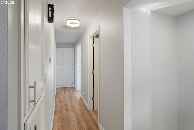 hallway with a textured ceiling and light hardwood / wood-style floors