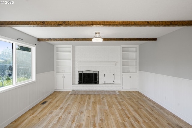 unfurnished living room with beamed ceiling, light wood-type flooring, built in shelves, and a fireplace