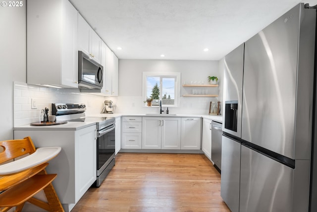 kitchen with a sink, decorative backsplash, light countertops, stainless steel appliances, and white cabinetry