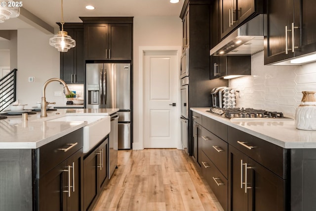 kitchen featuring pendant lighting, stainless steel appliances, light wood-style floors, light stone countertops, and under cabinet range hood