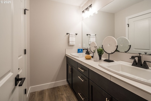 bathroom featuring double vanity, baseboards, a sink, and wood finished floors