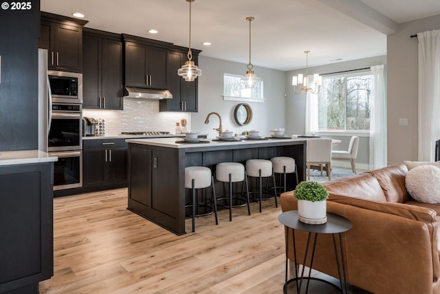 kitchen featuring stainless steel appliances, light countertops, hanging light fixtures, an island with sink, and a kitchen bar