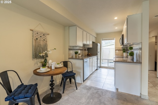 kitchen with a sink, backsplash, appliances with stainless steel finishes, light tile patterned floors, and light colored carpet