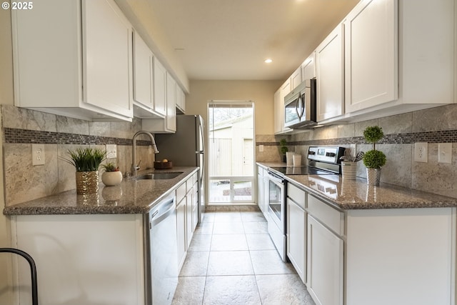 kitchen with dark stone counters, a sink, appliances with stainless steel finishes, white cabinetry, and tasteful backsplash