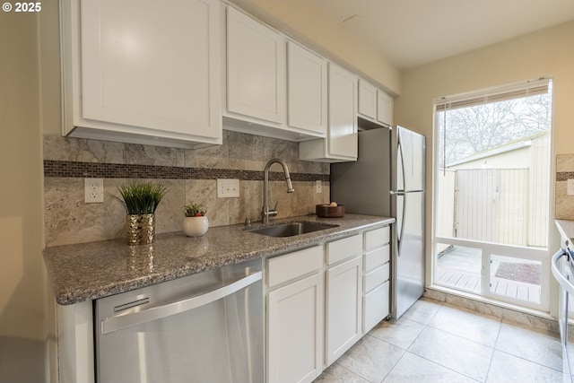 kitchen with dishwasher, dark stone counters, white cabinets, and a sink