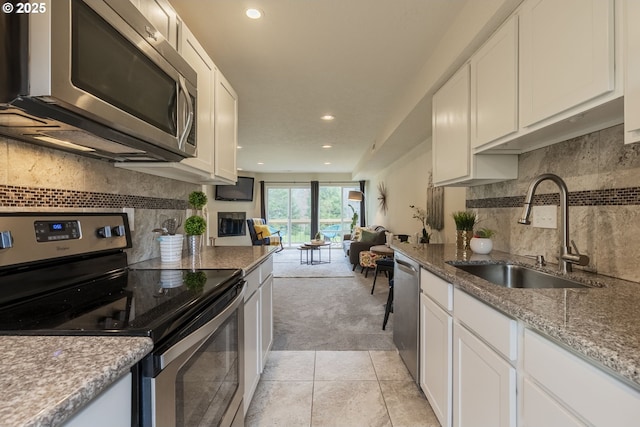 kitchen with a sink, open floor plan, stainless steel appliances, white cabinets, and light colored carpet