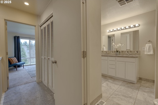 corridor with baseboards, light colored carpet, visible vents, and a sink