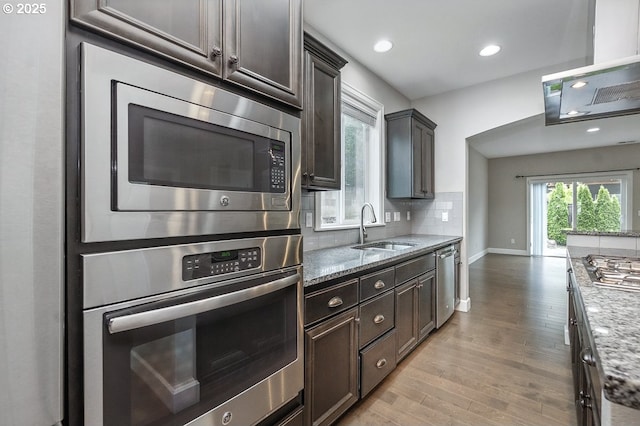 7698 NW Catalpa St, Portland, OR 97229 - kitchen with stainless steel appliances, a sink, light stone countertops, wood finished floors, and recessed lighting