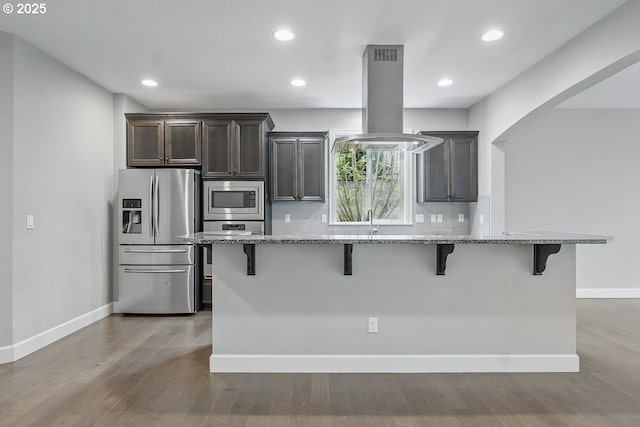 7698 NW Catalpa St, Portland, OR 97229 - kitchen featuring stainless steel appliances, island exhaust hood, a breakfast bar area, light stone countertops, and recessed lighting