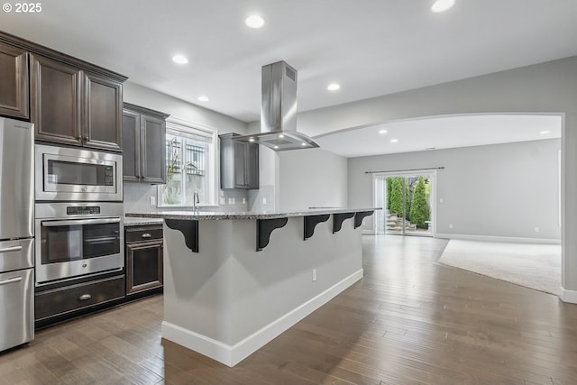 7698 NW Catalpa St, Portland, OR 97229 - kitchen with appliances with stainless steel finishes, island exhaust hood, a kitchen breakfast bar, light stone countertops, and open floor plan