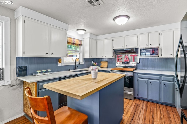 kitchen with appliances with stainless steel finishes, under cabinet range hood, a sink, wood finished floors, and white cabinetry