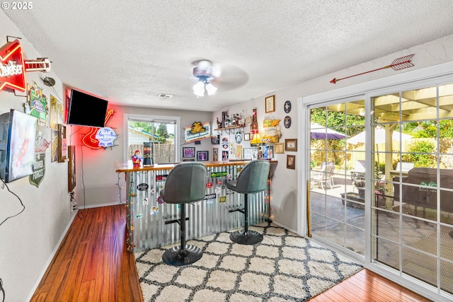 indoor dry bar with a textured ceiling, wood finished floors, baseboards, and a ceiling fan