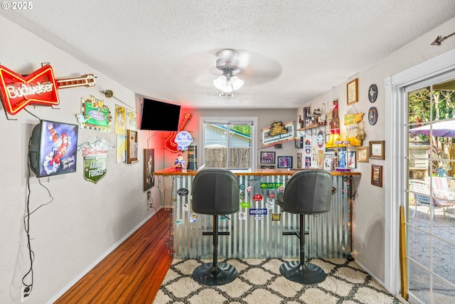 indoor dry bar featuring a textured ceiling, a ceiling fan, wood finished floors, and baseboards