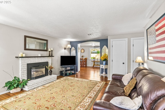 living room featuring wood finished floors, a textured ceiling, arched walkways, a glass covered fireplace, and baseboards