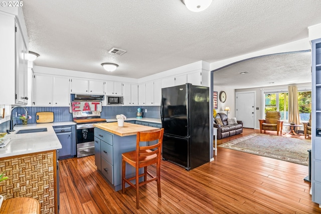 kitchen with appliances with stainless steel finishes, a sink, butcher block counters, under cabinet range hood, and a textured ceiling