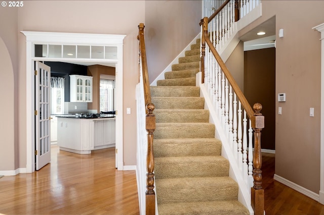 stairway with recessed lighting, a high ceiling, baseboards, and wood finished floors