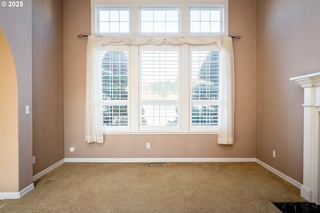 empty room featuring arched walkways, baseboards, visible vents, and carpet