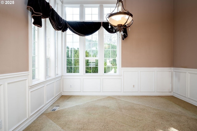 unfurnished dining area featuring carpet floors, wainscoting, visible vents, and a decorative wall