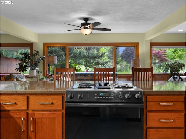 24880 E Arrah Wanna Blvd, Welches, OR 97067 - kitchen with black range with electric stovetop, a ceiling fan, brown cabinetry, healthy amount of natural light, and a textured ceiling