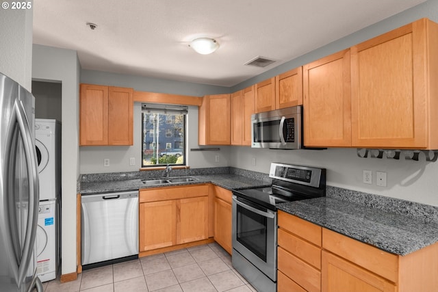 kitchen with sink, stainless steel appliances, light tile patterned flooring, light brown cabinetry, and dark stone counters