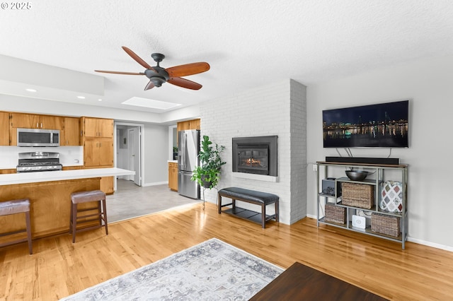 819 SE 98th Ave, Vancouver, WA 98664 - living room with a ceiling fan, light wood-type flooring, a brick fireplace, a textured ceiling, and a skylight