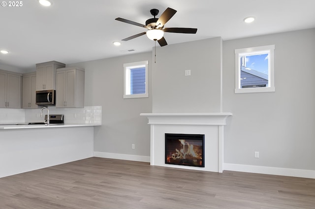 unfurnished living room featuring ceiling fan, plenty of natural light, sink, and light hardwood / wood-style flooring