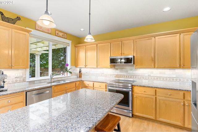 kitchen featuring a breakfast bar, sink, decorative light fixtures, appliances with stainless steel finishes, and light stone countertops