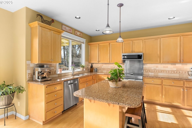 kitchen with appliances with stainless steel finishes, light brown cabinetry, sink, a center island, and light hardwood / wood-style floors