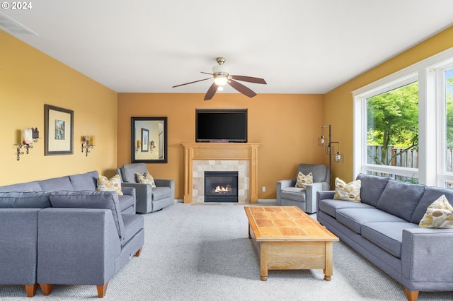 living room with a tile fireplace, light carpet, and ceiling fan