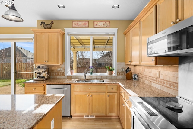 kitchen with a wealth of natural light, pendant lighting, sink, stainless steel appliances, and light stone countertops