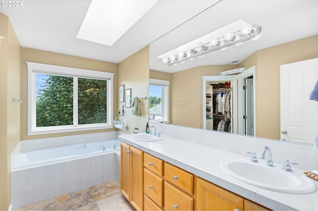 bathroom featuring vanity, a skylight, and tiled bath