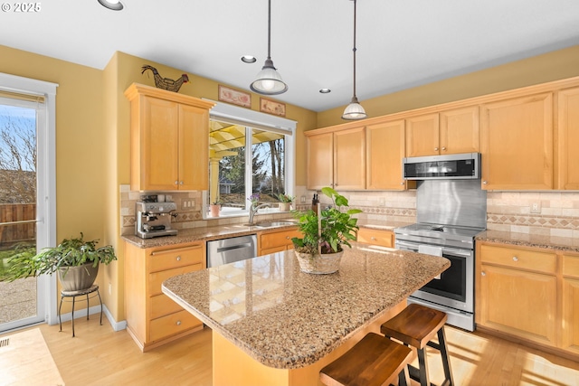 kitchen featuring pendant lighting, appliances with stainless steel finishes, a center island, light stone counters, and light brown cabinetry