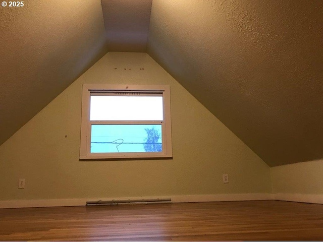 additional living space featuring baseboard heating, lofted ceiling, wood-type flooring, and a textured ceiling