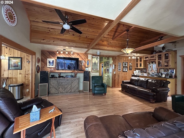 living area with wooden walls, vaulted ceiling with beams, wooden ceiling, wood finished floors, and a ceiling fan