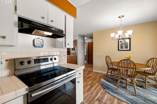 15870 SW Royalty Pkwy, King City, OR 97224 - kitchen featuring stainless steel electric range oven, tile counters, extractor fan, light wood-style floors, and white cabinetry