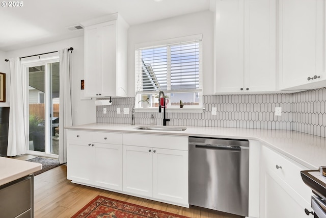 kitchen featuring stainless steel dishwasher, a sink, light wood-type flooring, tasteful backsplash, and light countertops